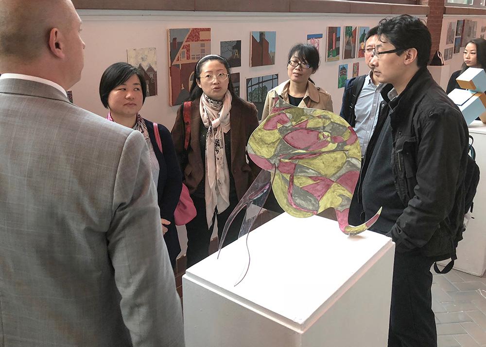 ”Multiple Visiting Scholars  team members look through the various pieces on display in an art gallery.”