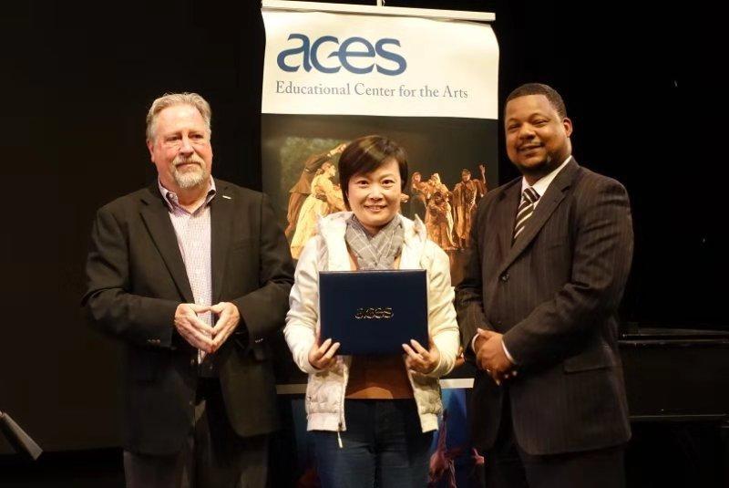 "Visiting Scholars and  ACES Leadership who is holding a gift pose for a photo in front of an ACES display.”