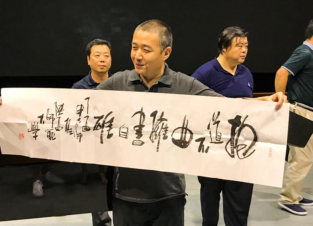"Visiting Scholars members hold up a wide piece of paper with Chinese characters.”