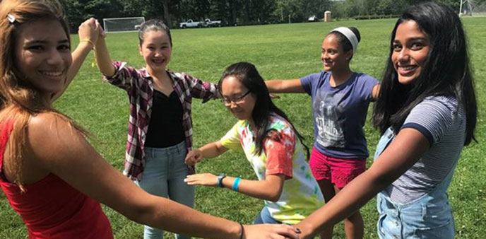 A group of young campers holding hands in a circle having fun.