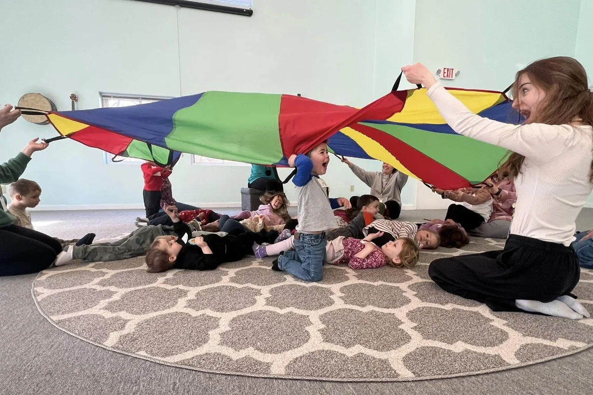 preschool students and teacher using floor parachute
