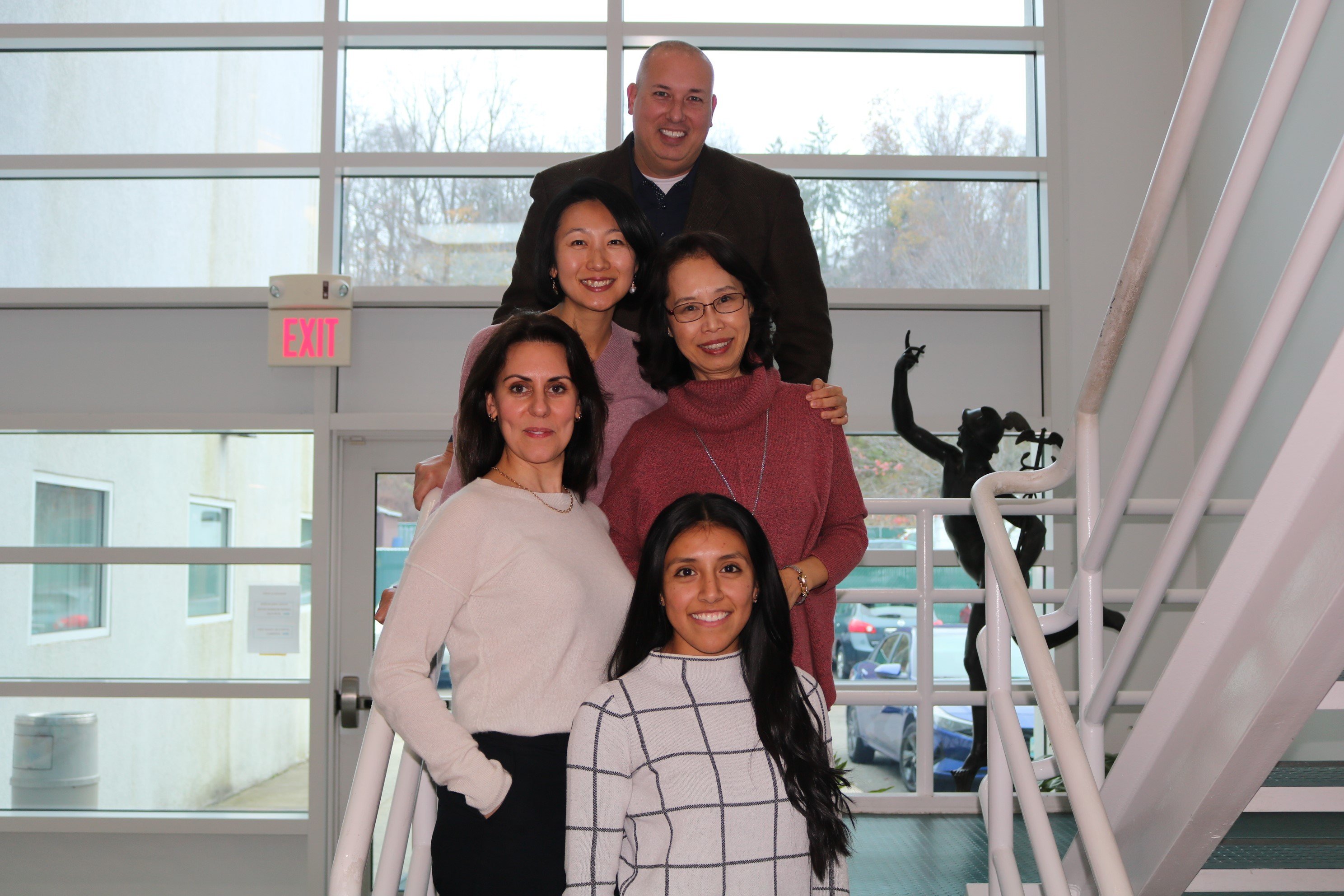 ACES International’s Staff, including Jason Hiruo, Meimei Zou, Grace Xie, Melissa Alers, and Angie Cedillo Pulla pose on a staircase for a photo.